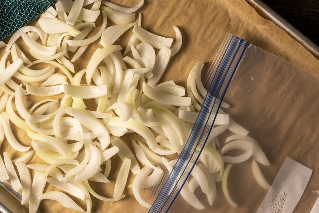 Frozen onions slivers being put into a freezer bag. 