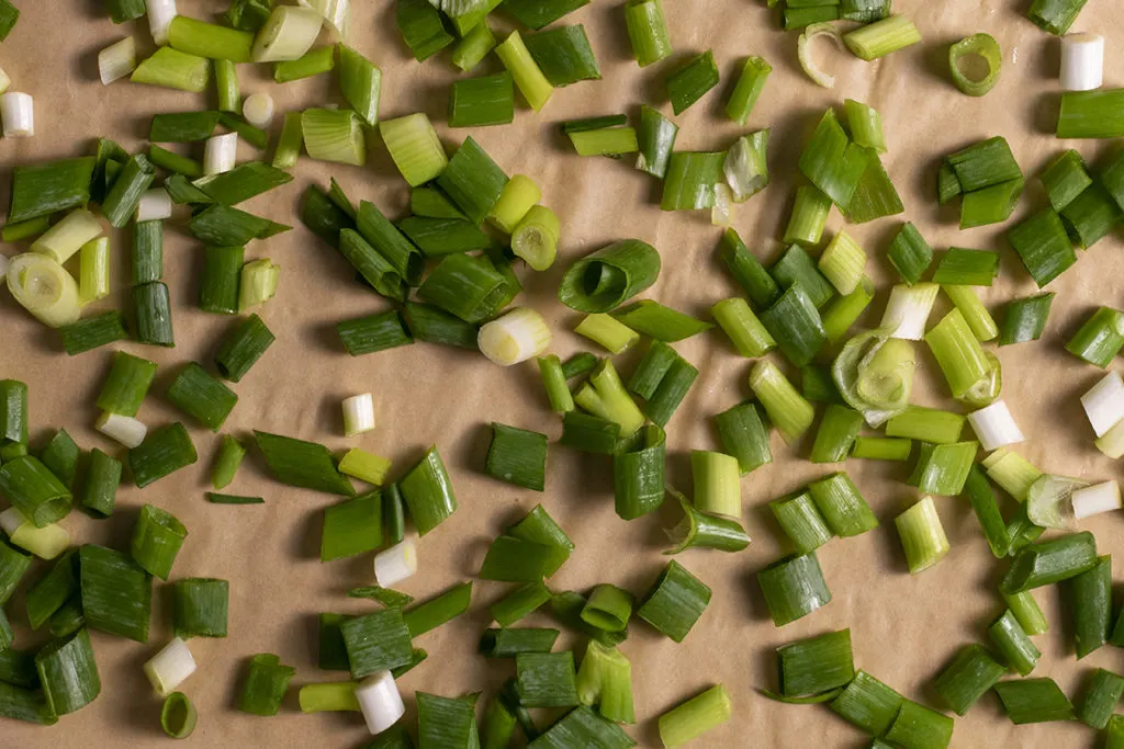 Overhead view of sliced green onions on a parchment lined baking sheet. 