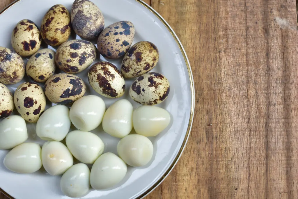 Hard-boiled quail eggs, both peeled and unpeeled on a plate. 