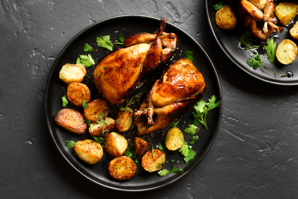 a plate with two roasted quail and roasted potatoes on it.