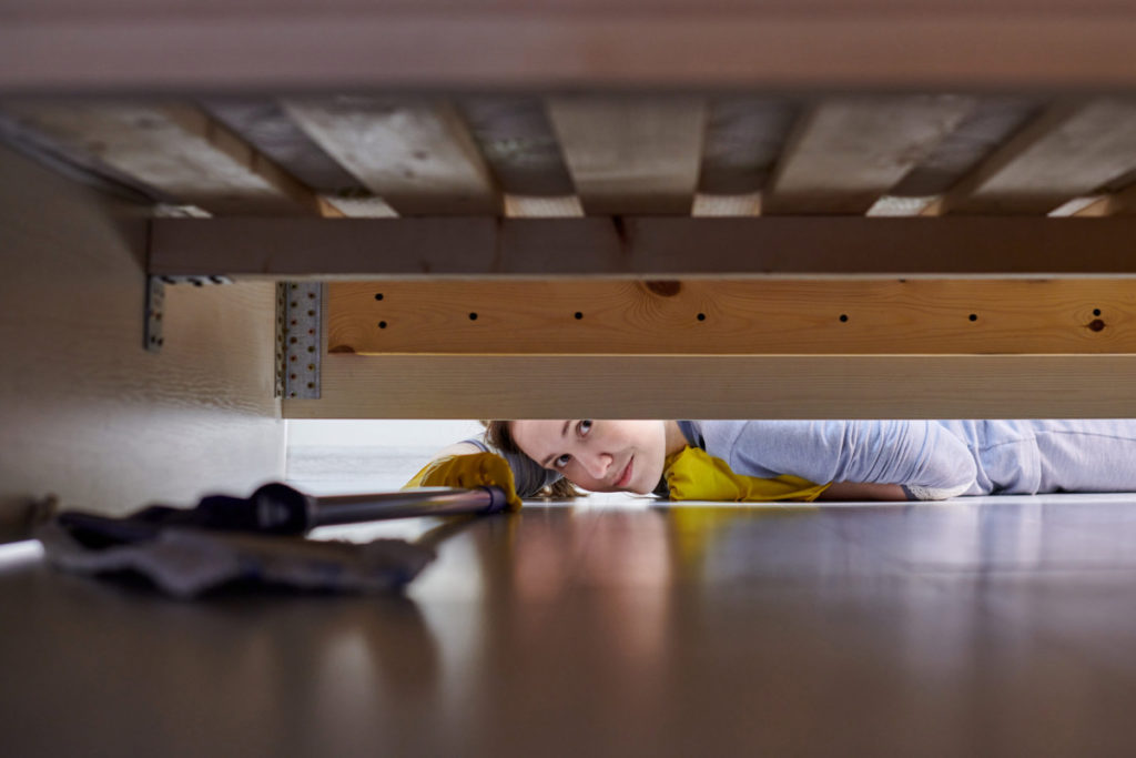 A woman dusting under a bed. 