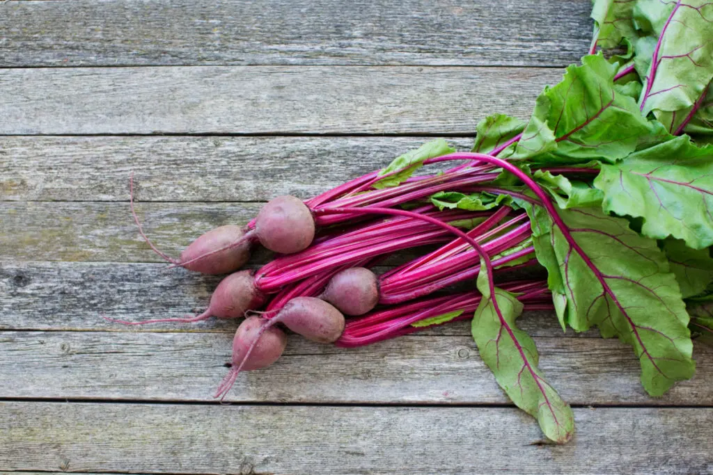 A bunch of small beets on a weathered wood floor.