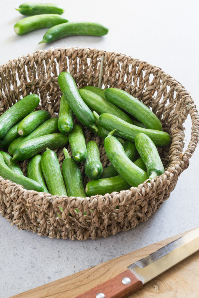 A woven basket filled with cocktail cucumbers. 