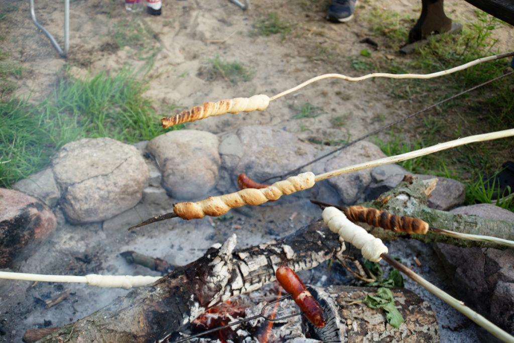 People holding sticks over a campfire and cooking pigs in a blanket.