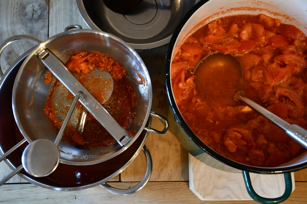 Overhead view of a pot of stewed tomatoes and a food mill with tomatoes in it. 