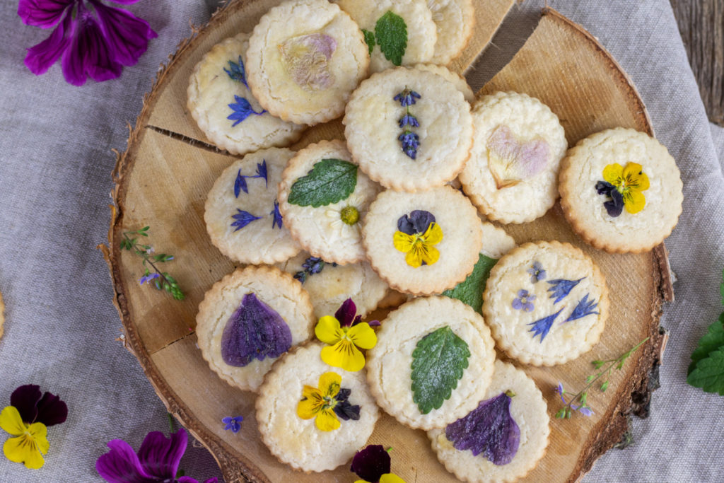 Shortbread cookies on a wood plank. The cookies have lemon balm leaves and other flower petals pressed into them.