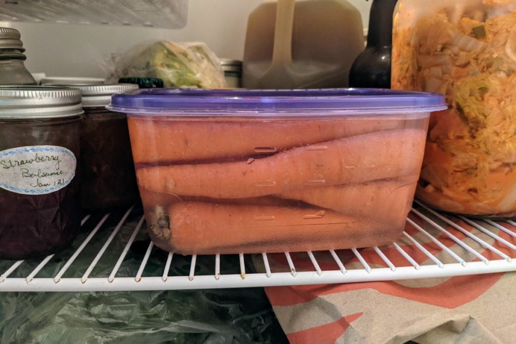 A plastic tub filled with carrots and water in a fridge. 