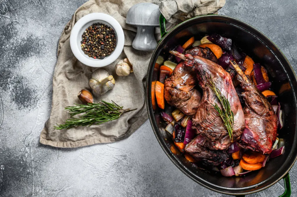 roasting pan with a roast rabbit, carrots, onions and peppers.