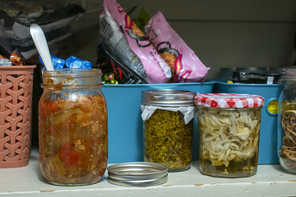 A photo of a jar of opened ratatouille with a spoon sticking out of it sitting on a shelf in the pantry.