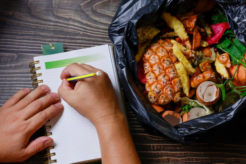hands writing in notebook next to a bag of spoiled food