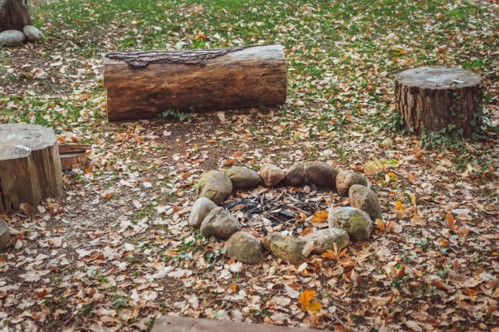 A rustic rock campfire ring surrounded by log stumps.