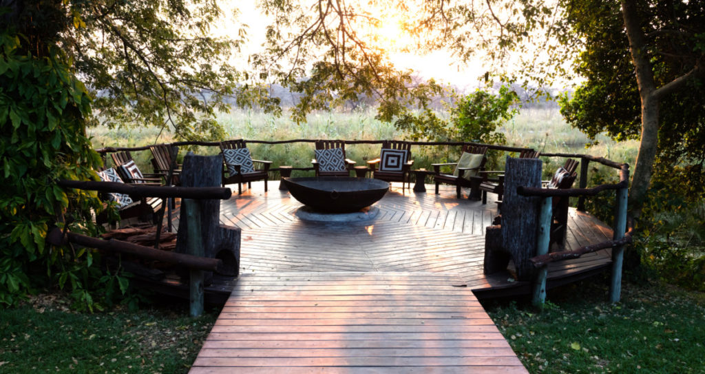 A round wood patio with a fire pit in the center, surrounded by wooden chairs.