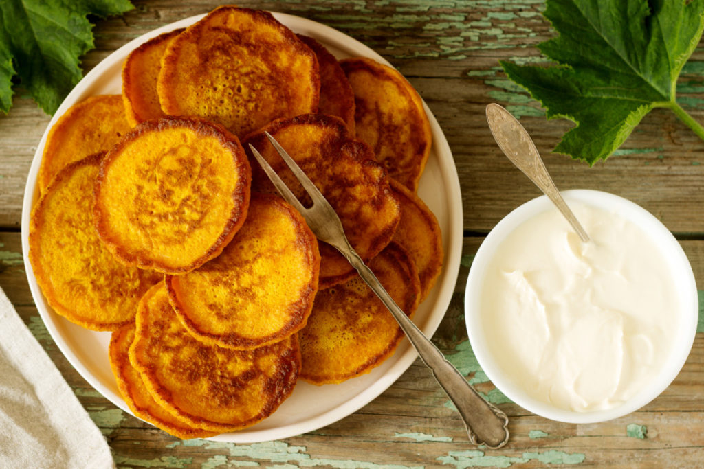 Flat lay of squash pancakes on a plate with a dish of cream next to them.
