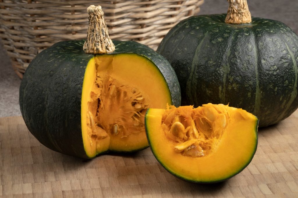 Dark green kabocha squash in the background and one in the foreground with a large chunk cut out of it to reveal the bright orange flesh.
