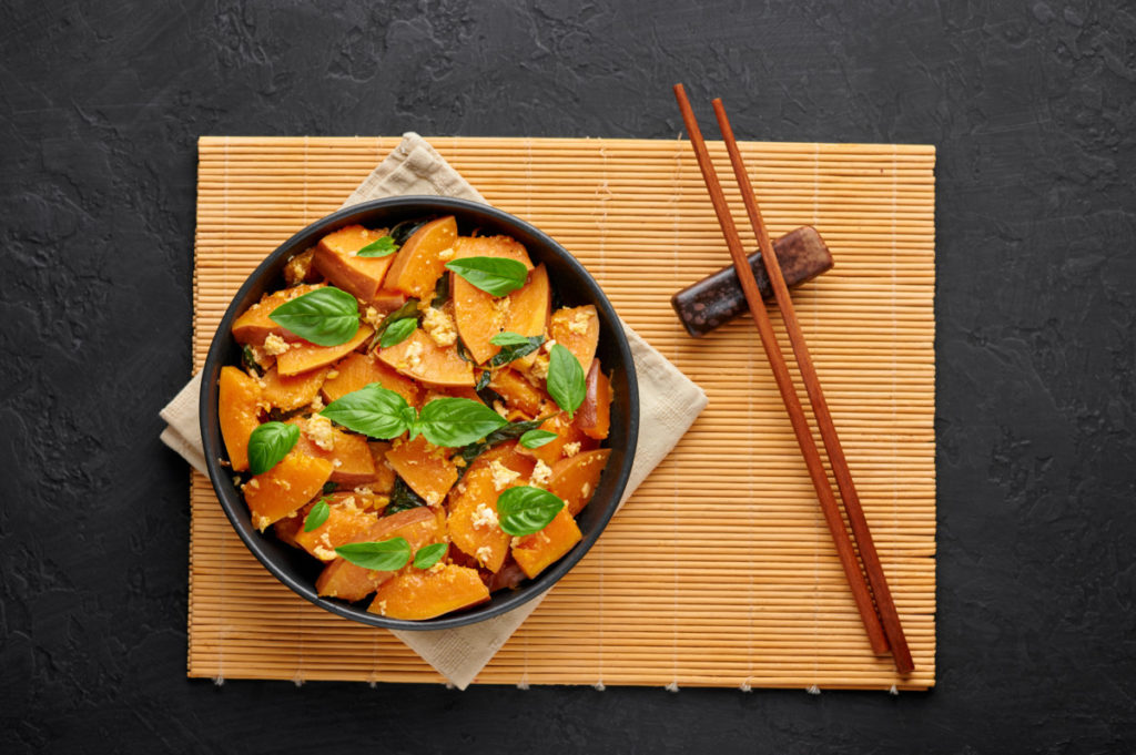 Stir fried kabocha squash with basil leaves in a bowl. chopsticks on a bamboo placemat