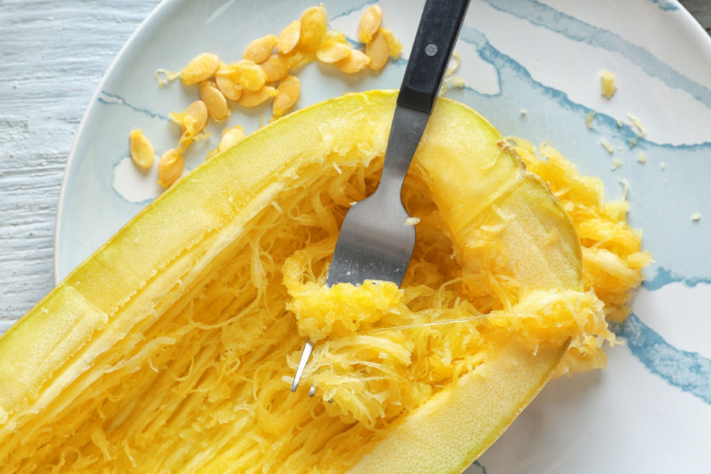 Half of a spaghetti squash with a fork resting on it where it's been used to shred the squash
