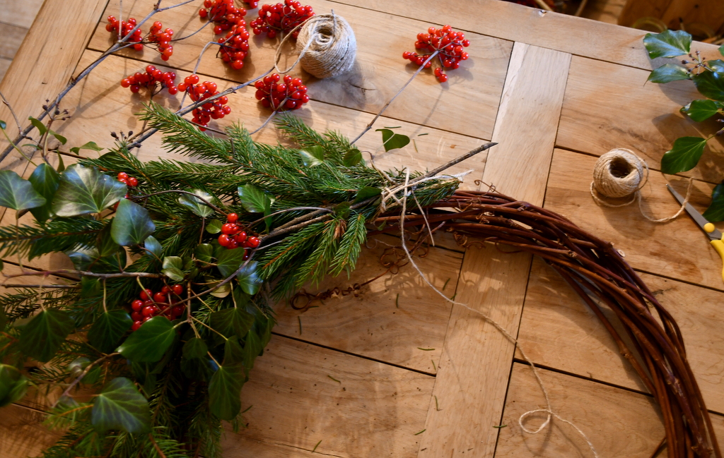 More bundles of greenery tied to same wreath with red berries added