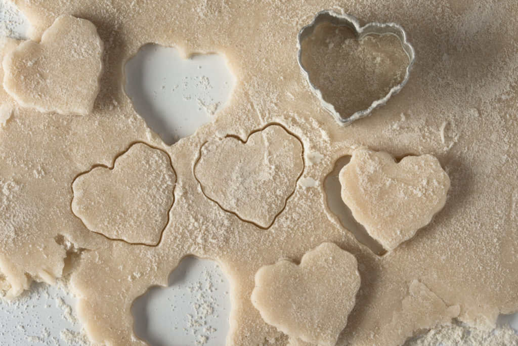 Cookie dough with heart shapes cut into them by a metal heart-shaped cookie cutter. 