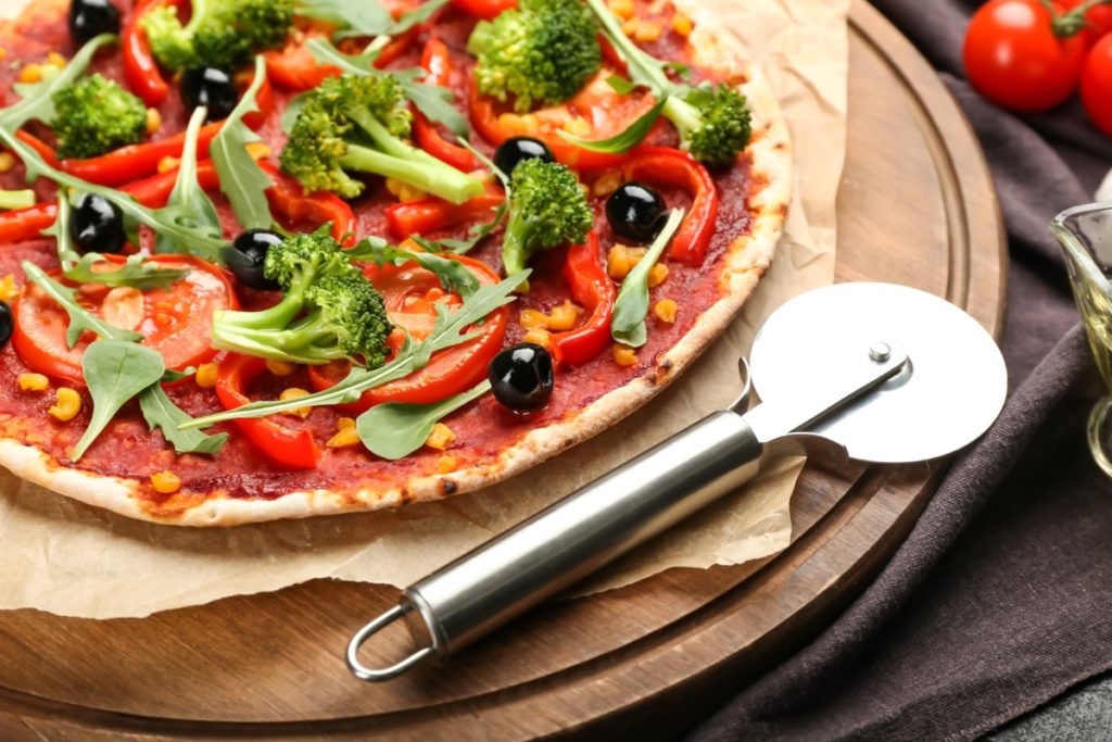 a pizza slicer on a cutting board with a freshly made pizza