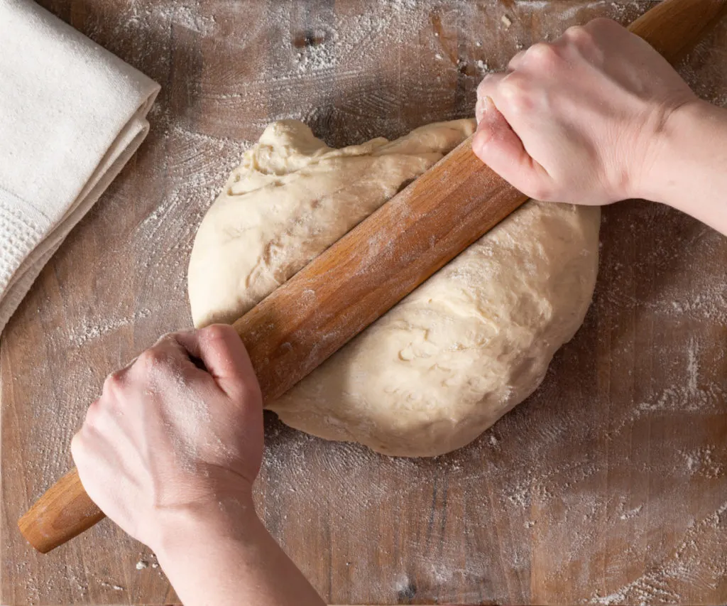 woman using a French rolling pin on a ball of dough.