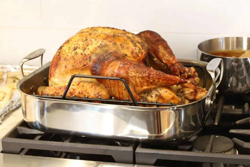 A roasted turkey resting in a stainless steel roasting pan on top of a stove.