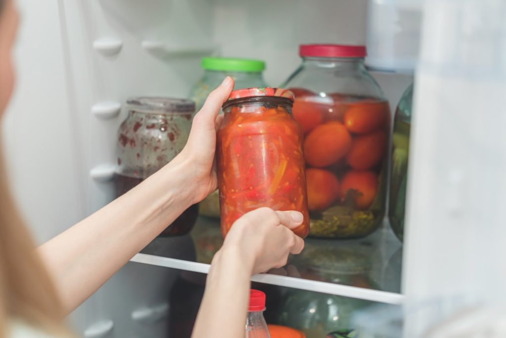 woman putting soup in a jar in fridge.