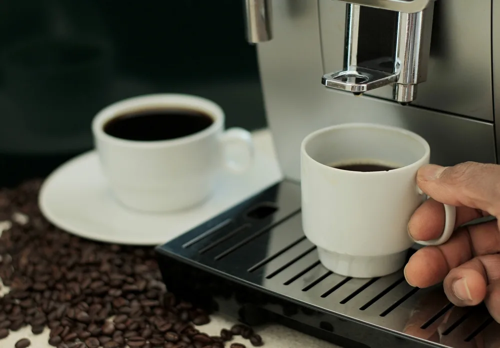Hand holding espresso cup under spout of espresso machine.