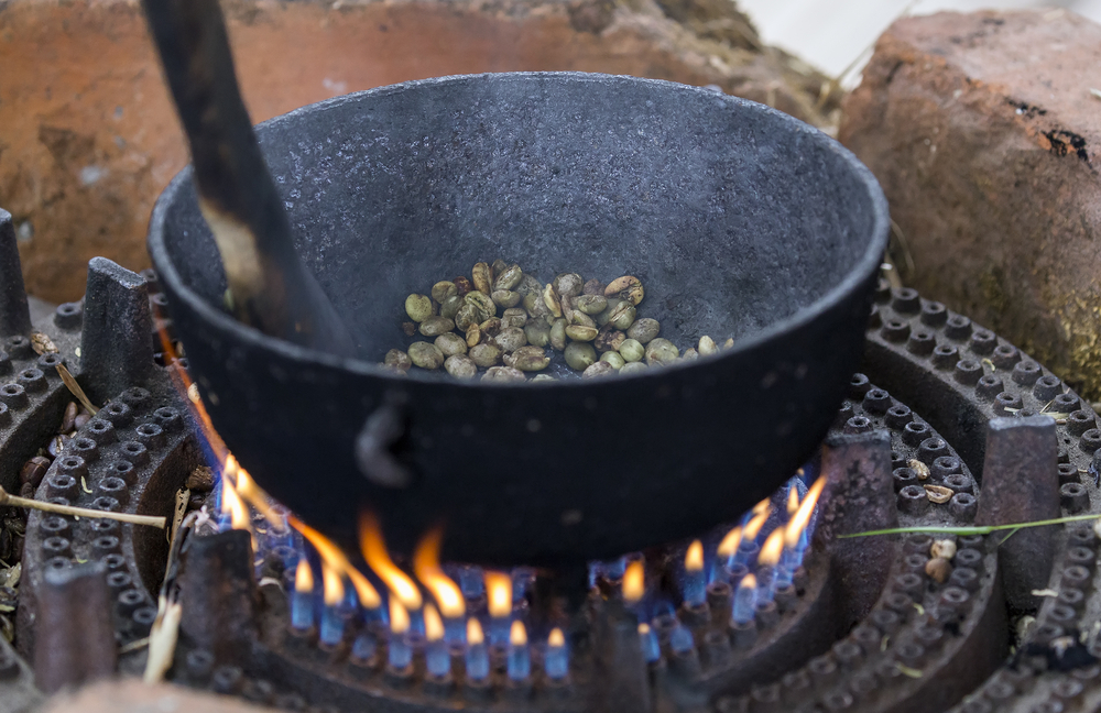 Cast iron pan holding coffee beans being roasted over an open flame.