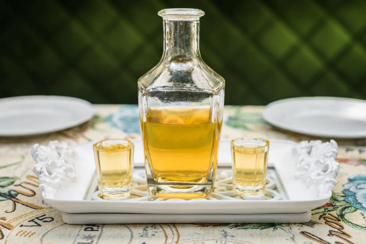 A small bottle filled with chamomile cordial, two tiny cordial glasses with cordial in them on either side.
