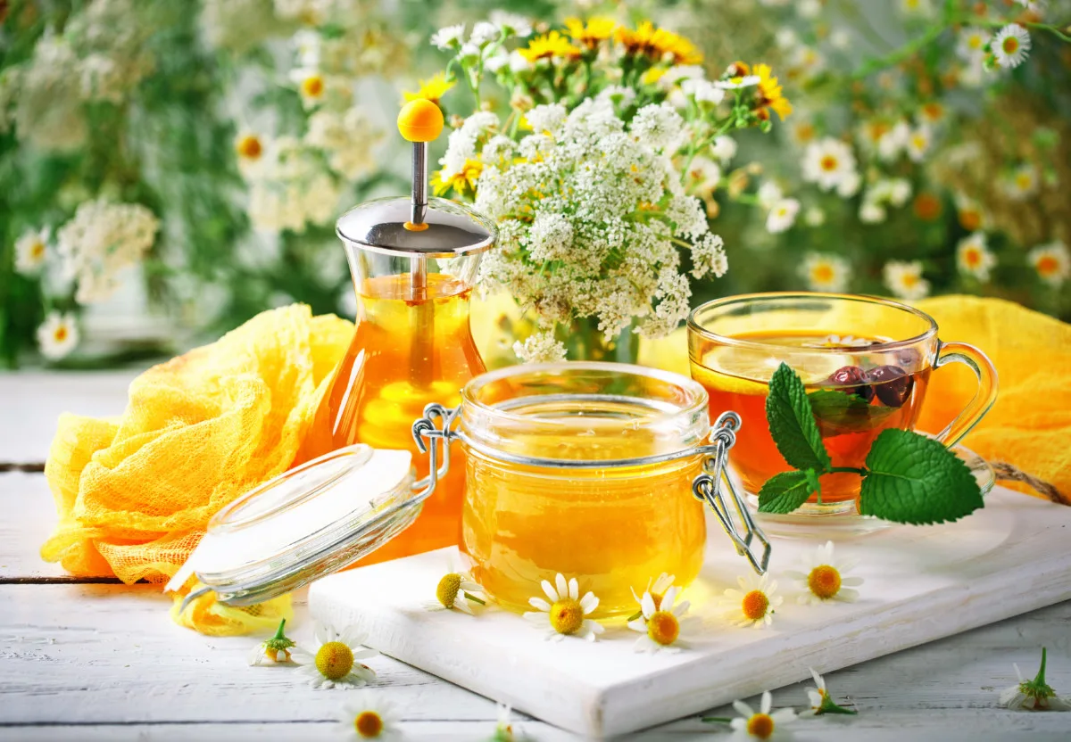A jar of chamomile jelly by a honey jar and a cup of tea.