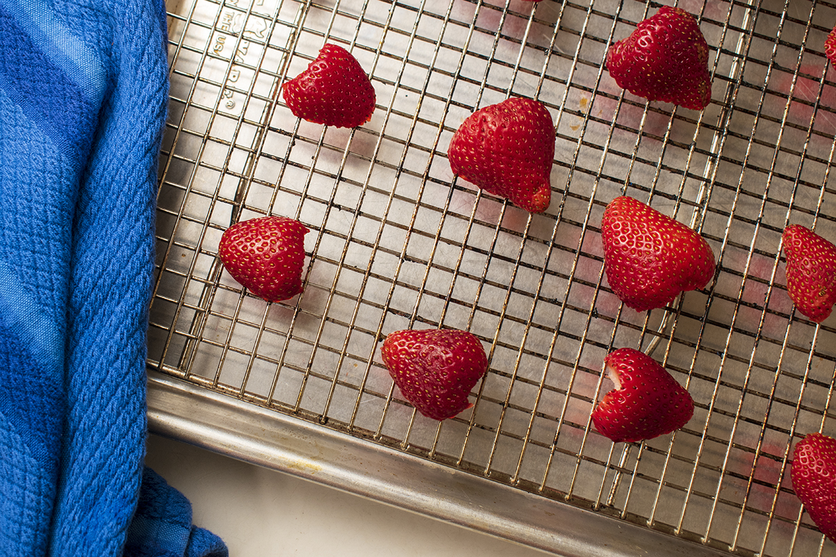 Halved strawberries on cooling rack on top of baking sheet