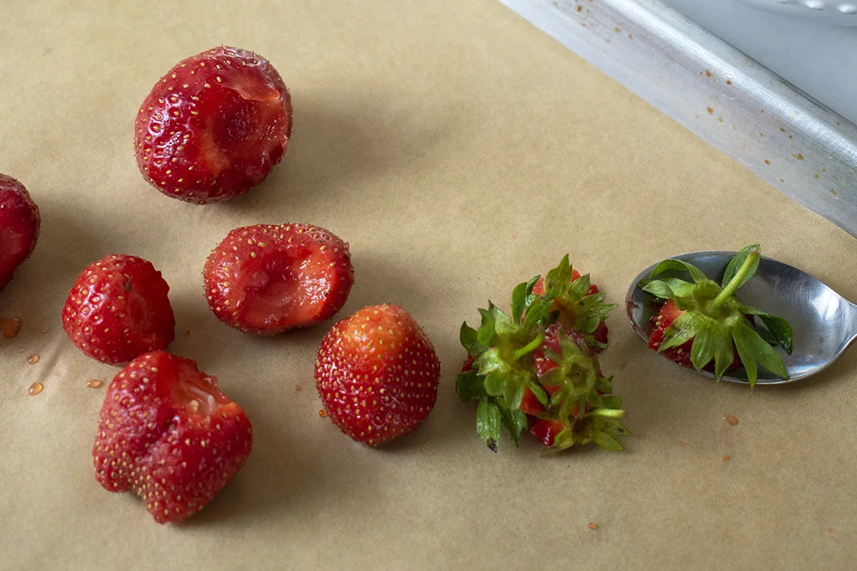 Strawberries on parchment paper, spoon used to remove their tops.