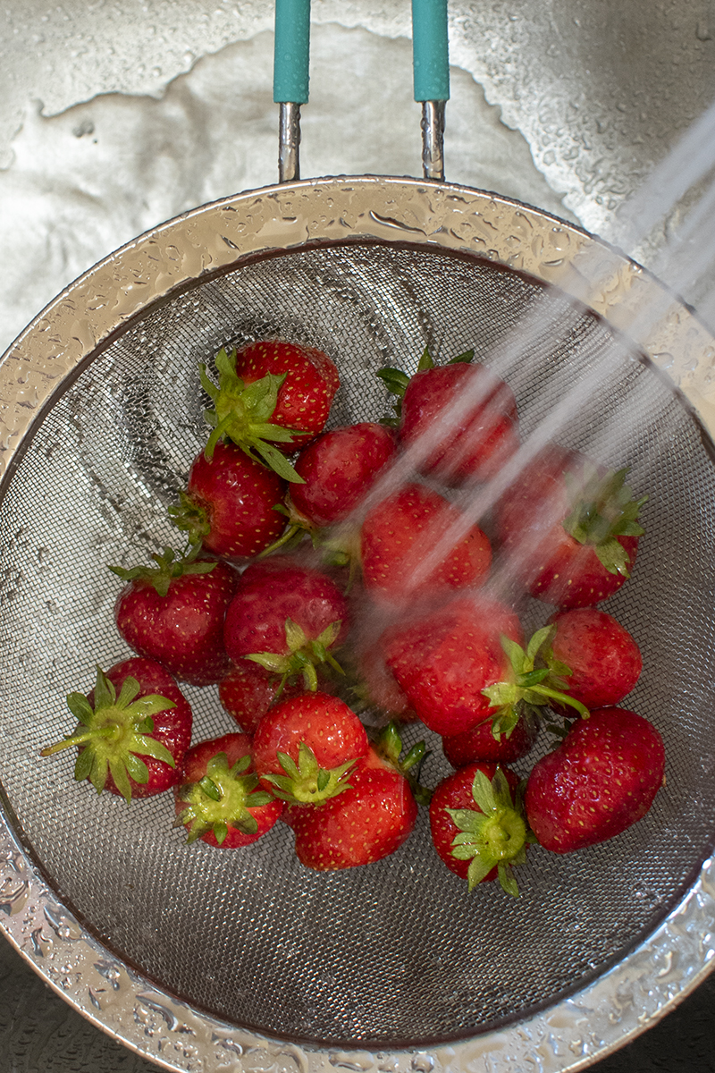 Mesh colander holding strawberries in sink, berries sprayed with water.