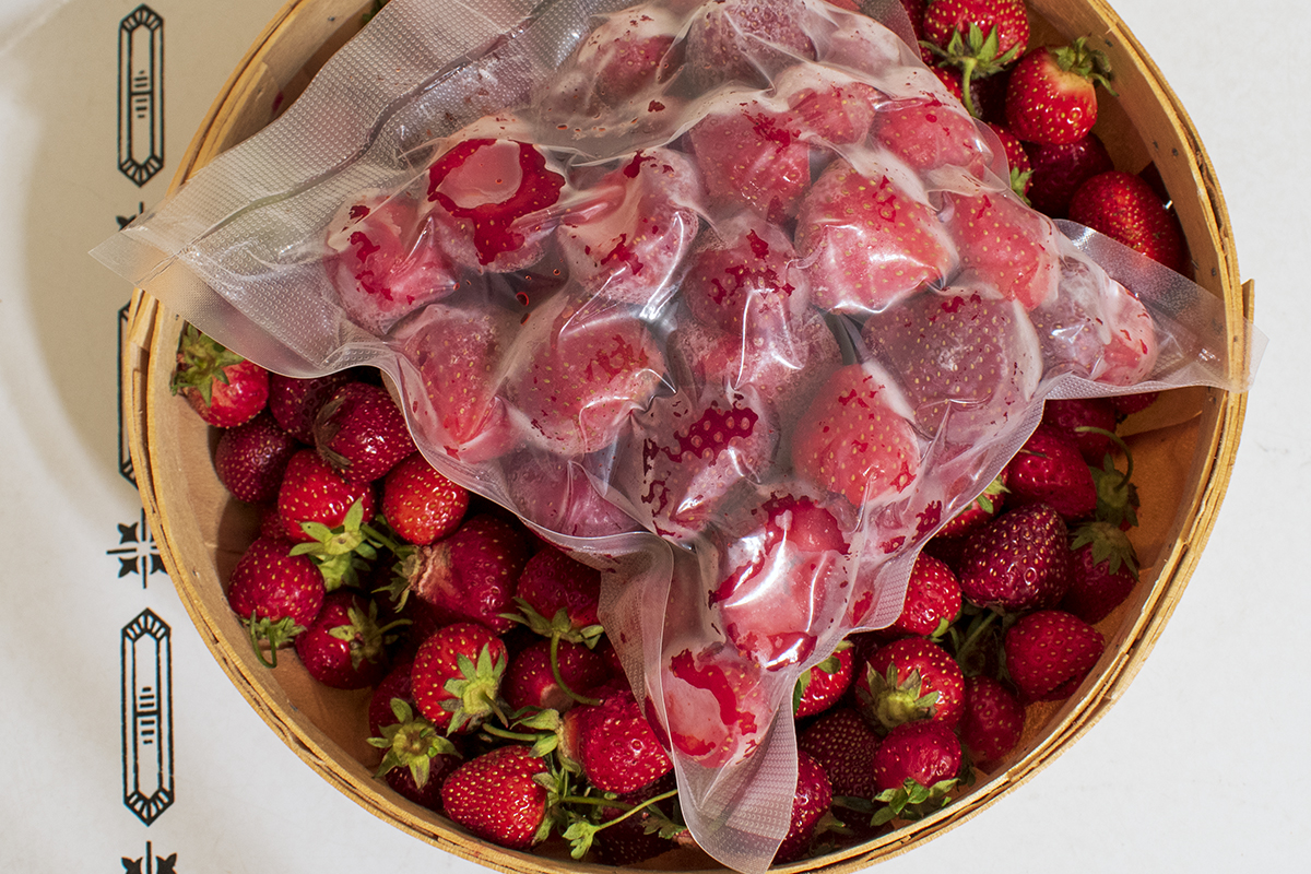 A bag of frozen strawberries atop a basket of strawberries.