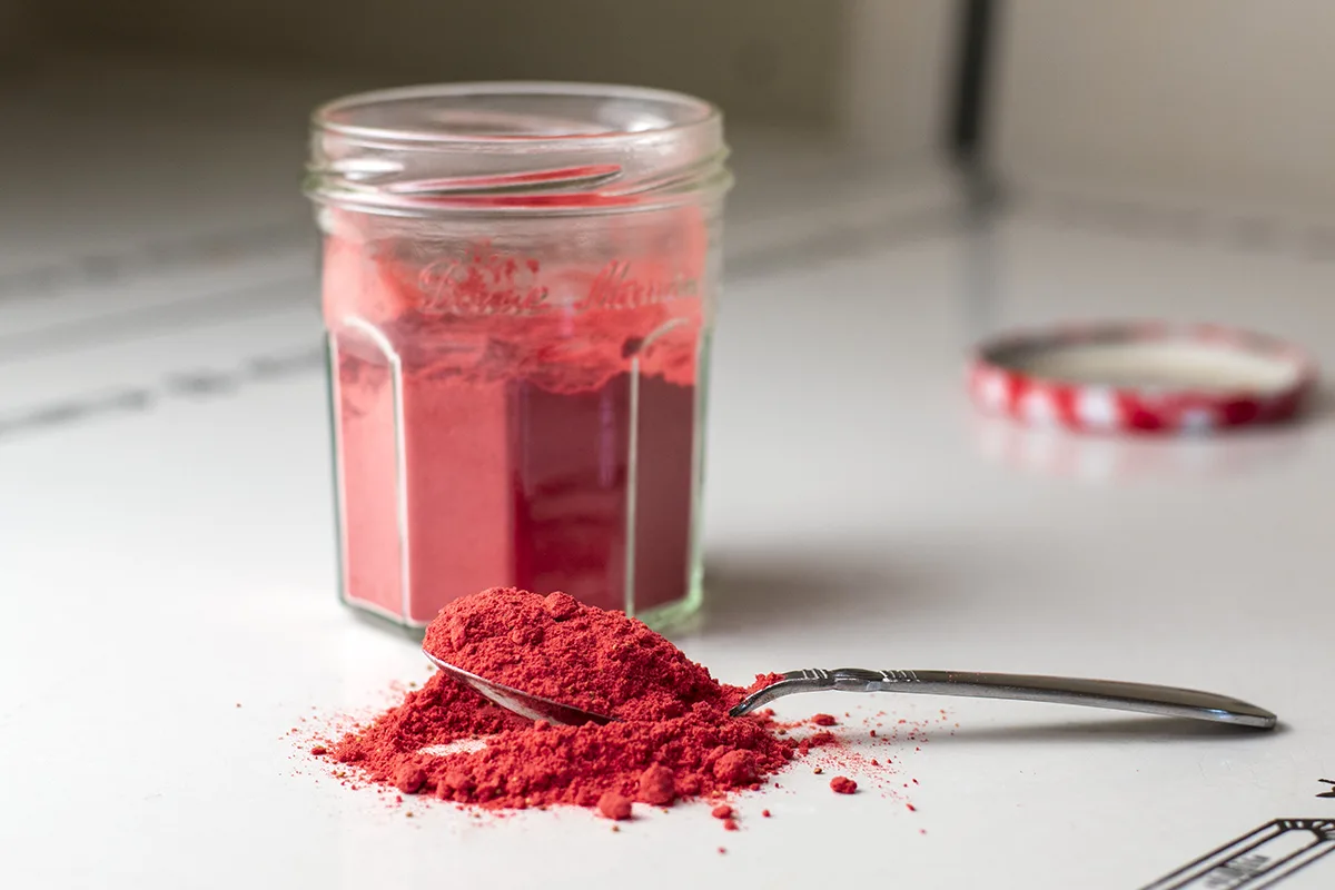 Heaping teaspoon of strawberry powder on a table, jar of strawberry powder in background