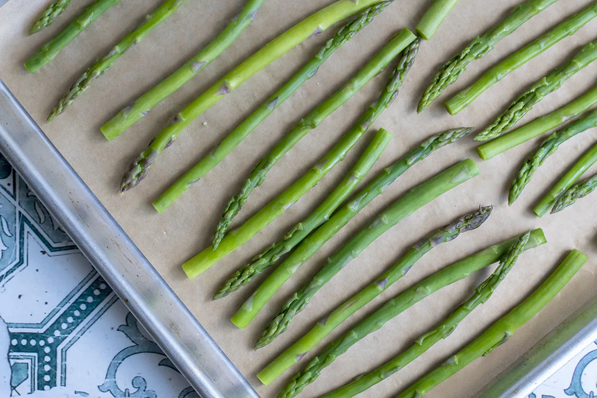 Overhead view of parchment lined baking sheet with blanched asparagus stems ready for freezing.