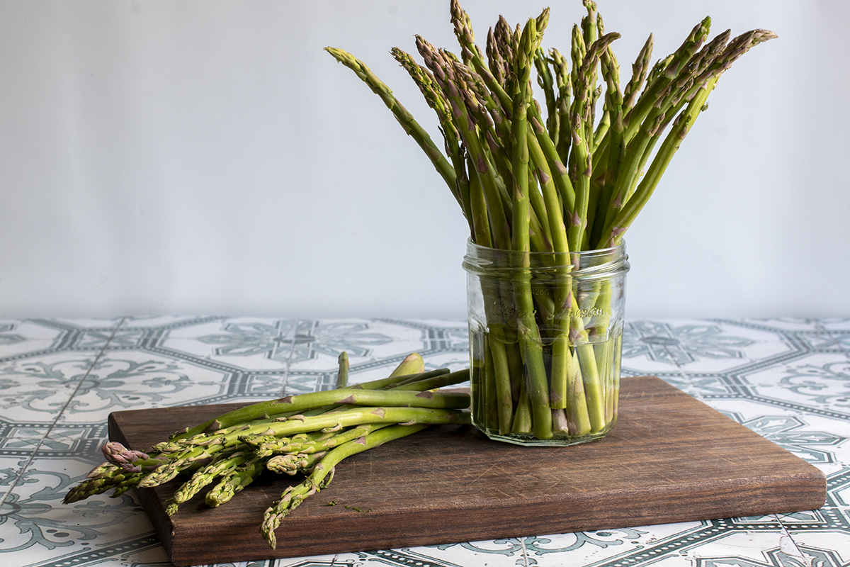 Asparagus stems on a cutting board and some in a jar of water. 