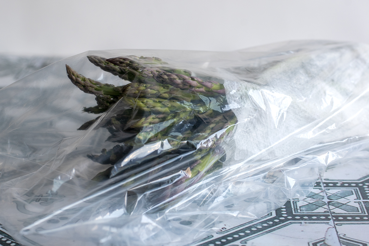 Asparagus stems wrapped in a damp paper towel and placed in an open plastic bag.