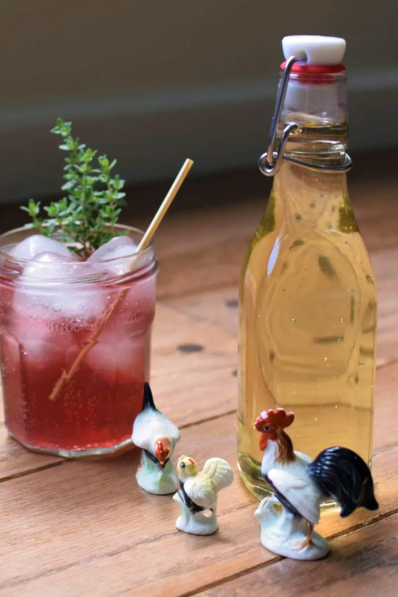 A bottle of thyme syrup next to a cocktail