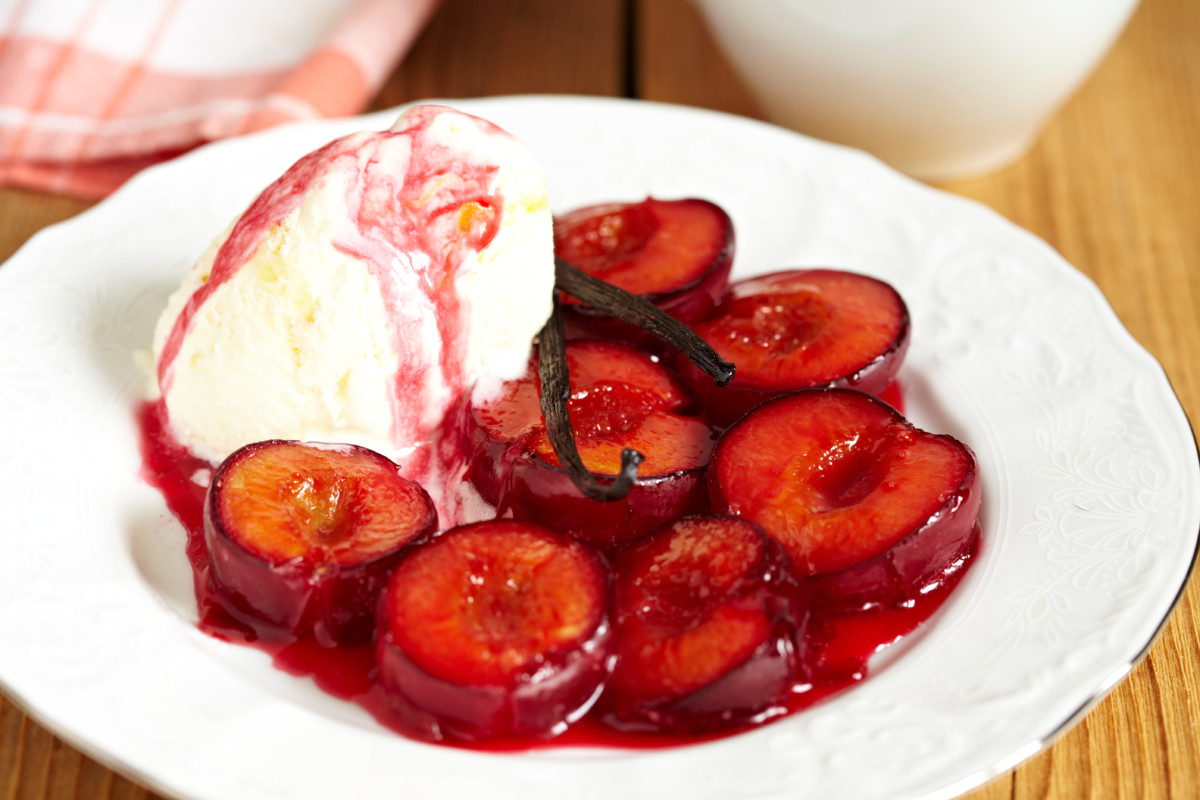 A bowl of poached plums with ice cream.