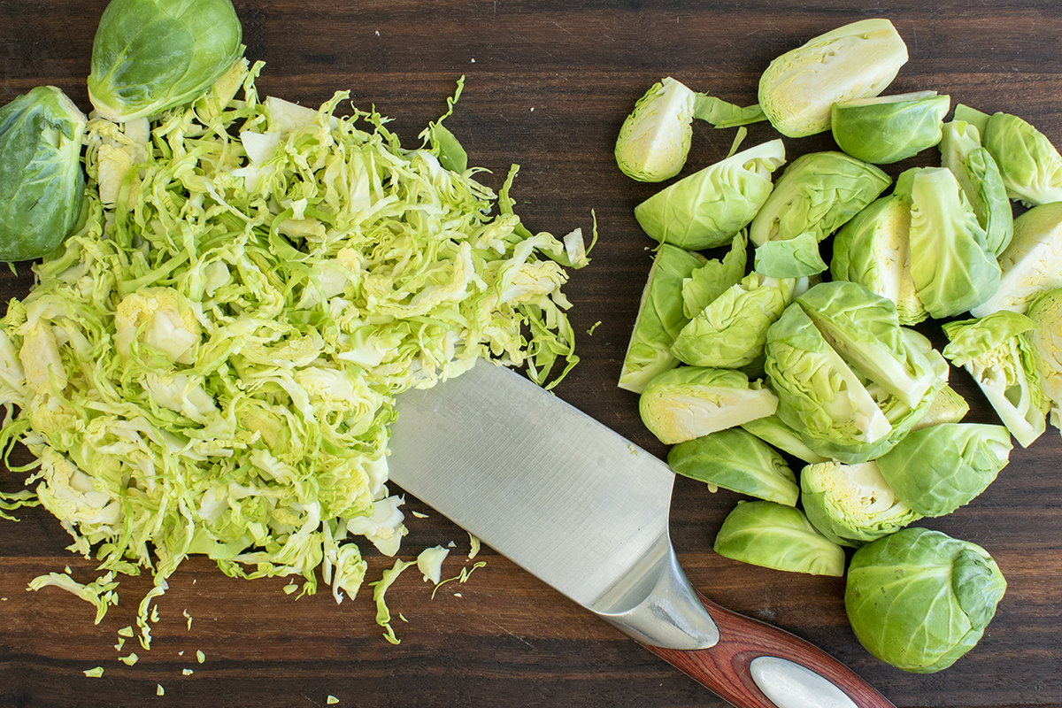 Overhead view of a cutting board with both shredded and quartered Brussels sprouts.