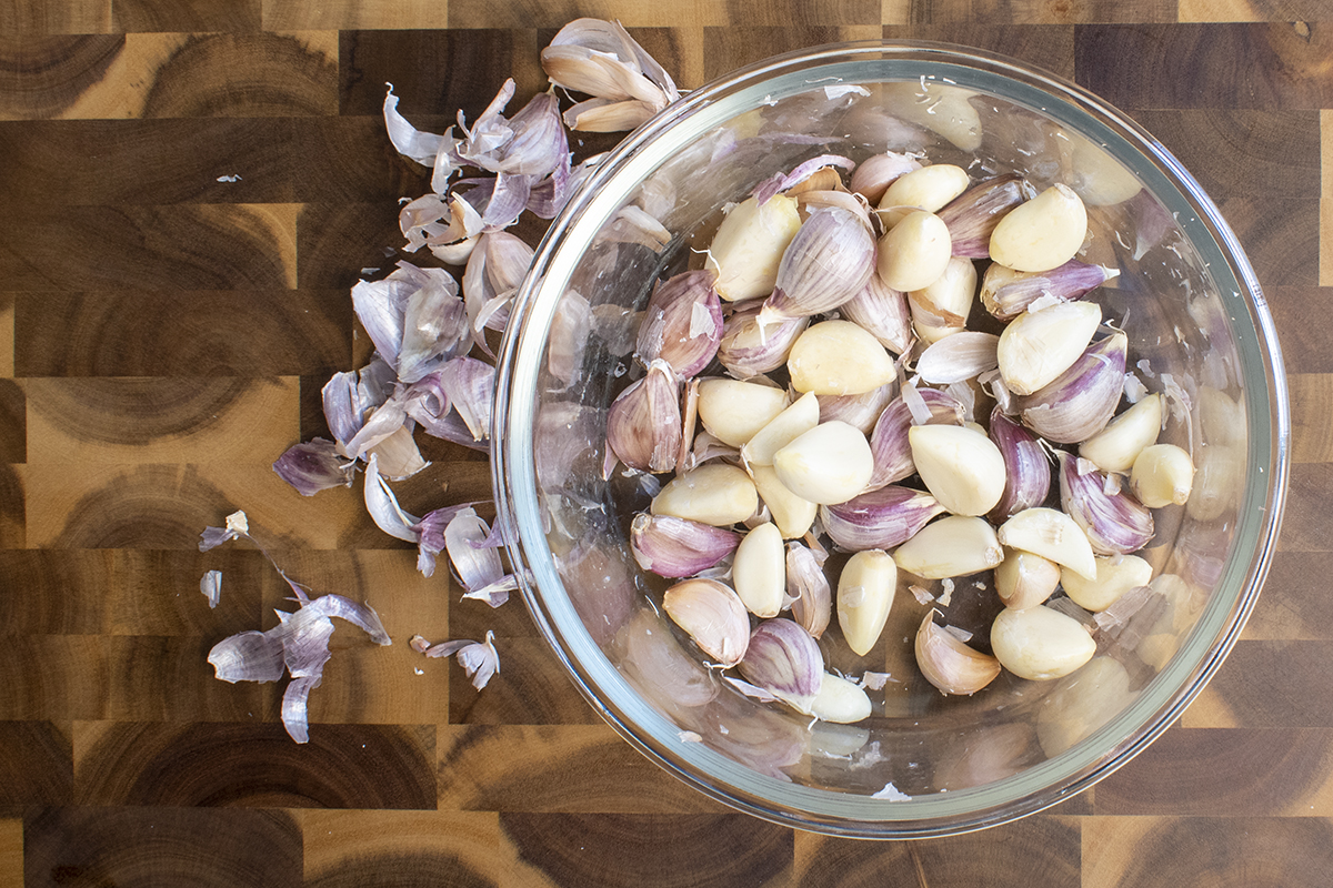 A glass bowl filled with mostly peeled garlic cloves. 