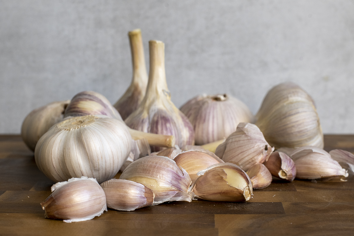 Garlic bulbs on a cutting board in front of a gray background