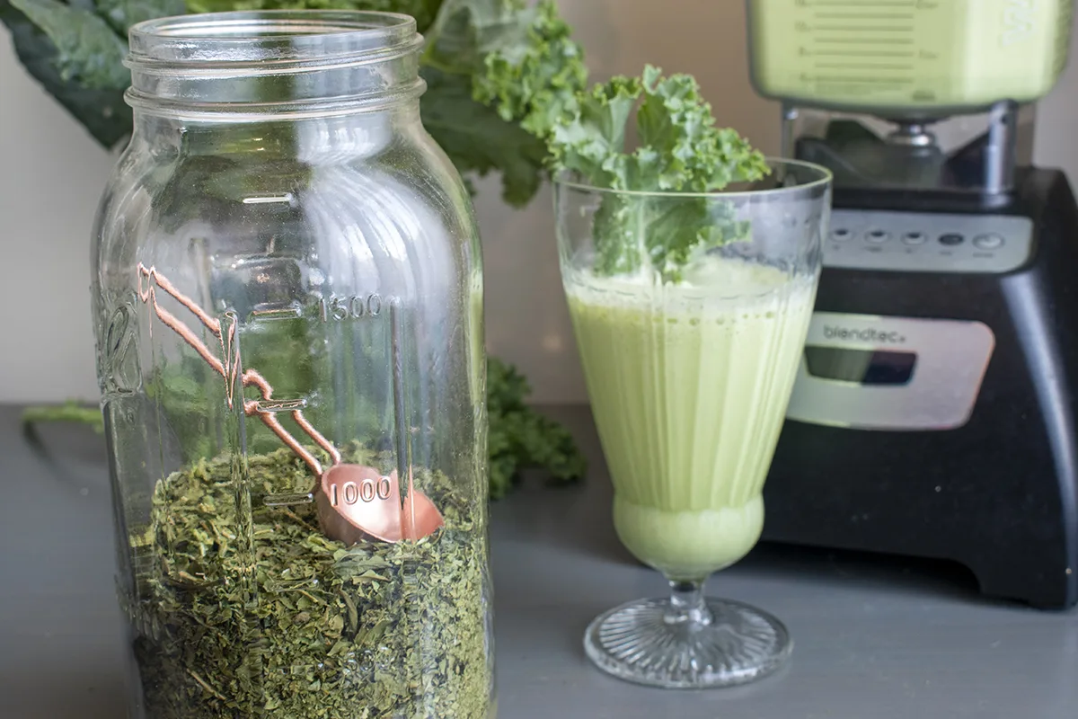 Jar filled with dried smoothie greens, blender and green smoothie in soft focus in back