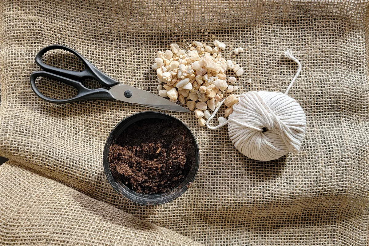 Overhead view of burlap, string, scissors, pebbles and soil-less potting mix. 