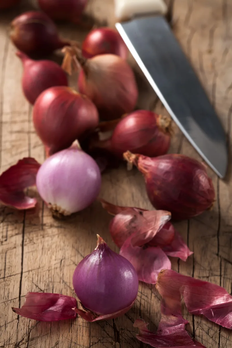 Cutting board with red pearl onions and a knife.