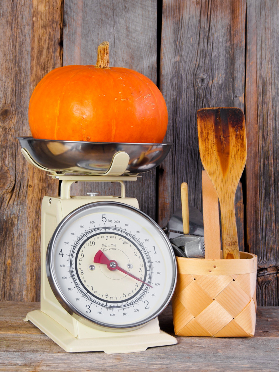 A bright orange pumpkin sitting on a kitchen scale with a rustic wooden background.