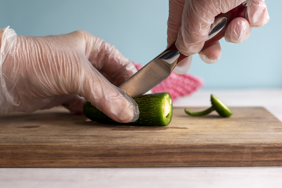 Gloved hands slicing a jalapeno pepper

