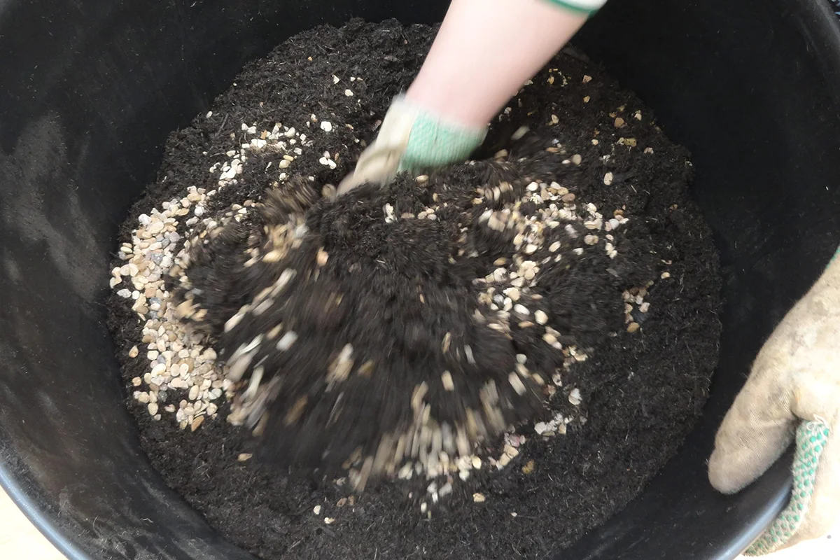 Woman's hands, wearing gloves mixing horticultural grit and peat-free compost.
