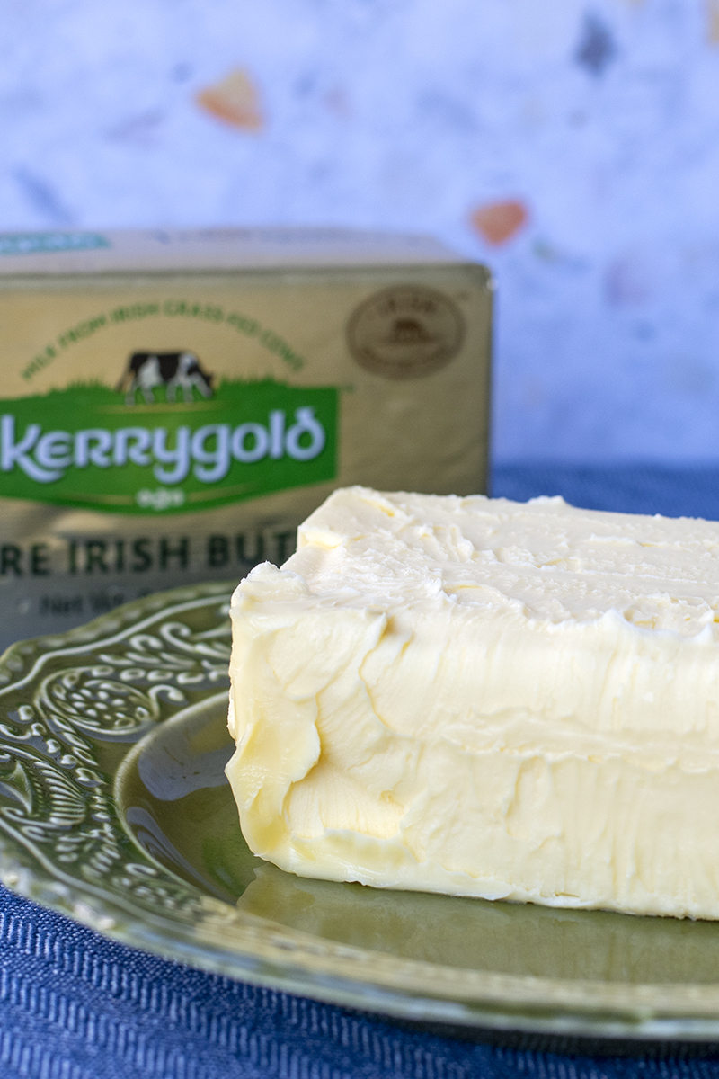 A block of butter on a plate with a wrapped package of Kerrygold butter in the background. 